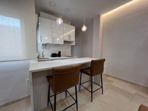 Eine moderne Küche mit weißem Arbeitsplatz, zwei Barhocker und Pendelleuchten.