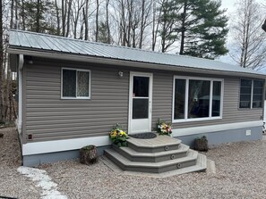 A single-story house with a grey exterior, white trim, and a front porch with steps leading to a door.