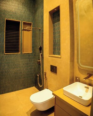 Une salle de bain comprenant des toilettes, un lavabo, une douche avec un pommeau de douche amovible et une fenêtre avec des stores.