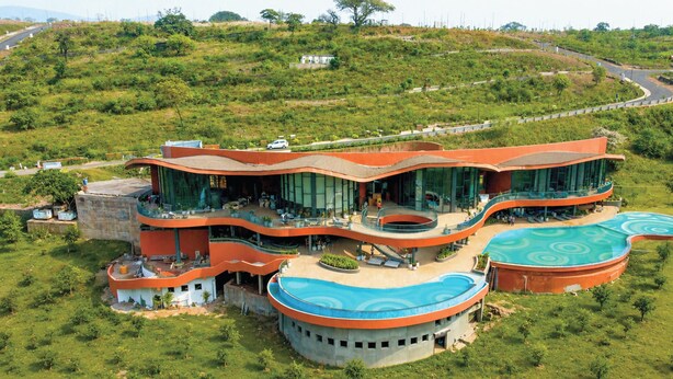 Un hotel moderno de varios niveles, con piscina, rodeado de exuberante vegetación.