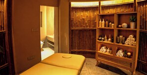 Une salle de spa équipée d’une table de massage, d’étagères contenant des produits de toilette et d’un mur en bambou.
