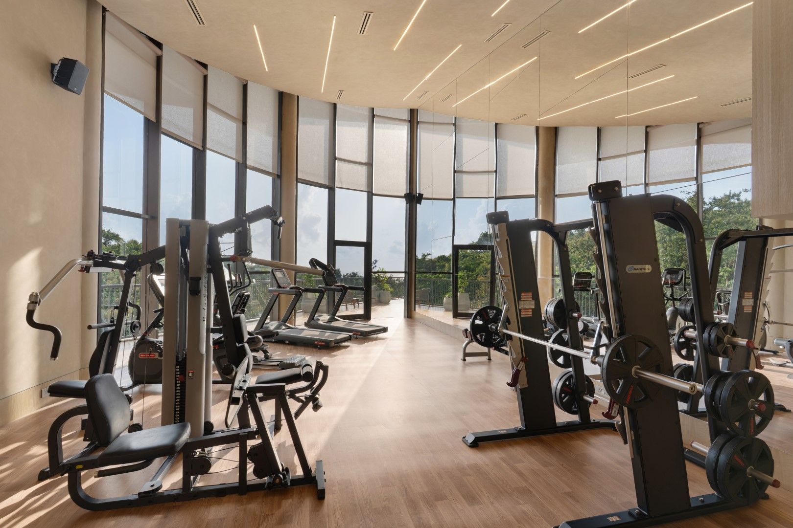 Une salle de sport équipée de machines de cardio, d’appareils de musculation et de grandes fenêtres donnant sur l’extérieur.