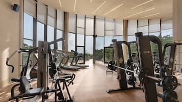 Une salle de sport équipée de machines de cardio, d’appareils de musculation et de grandes fenêtres donnant sur l’extérieur.