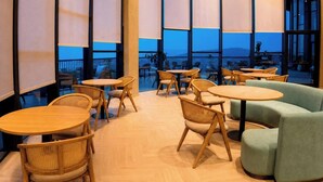 Un interior moderno con mesas redondas y sillas de mimbre, amplias ventanas que dan a una vista del exterior.