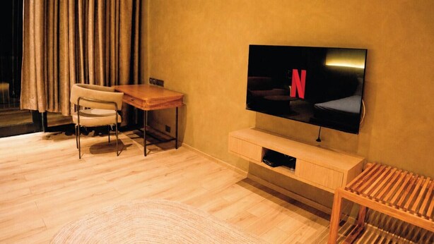 A modern living room with a flat-screen TV mounted on the wall, a wooden desk, a chair, and a small wooden bench. - Tomorrow Land by Miros - Anjarle (Dapoli)