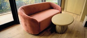 Habitació amb un sofà rosa, una taula rodona i vista per la finestra.