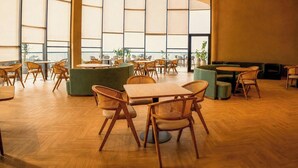 Un espacio interior amplio con diversas disposiciones de asientos, incluyendo mesas y sillas, y ventanas grandes que dejan entrar luz natural.