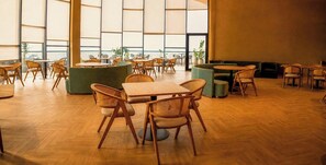 Un espacio interior amplio con diversas disposiciones de asientos, incluyendo mesas y sillas, y ventanas grandes que dejan entrar luz natural.