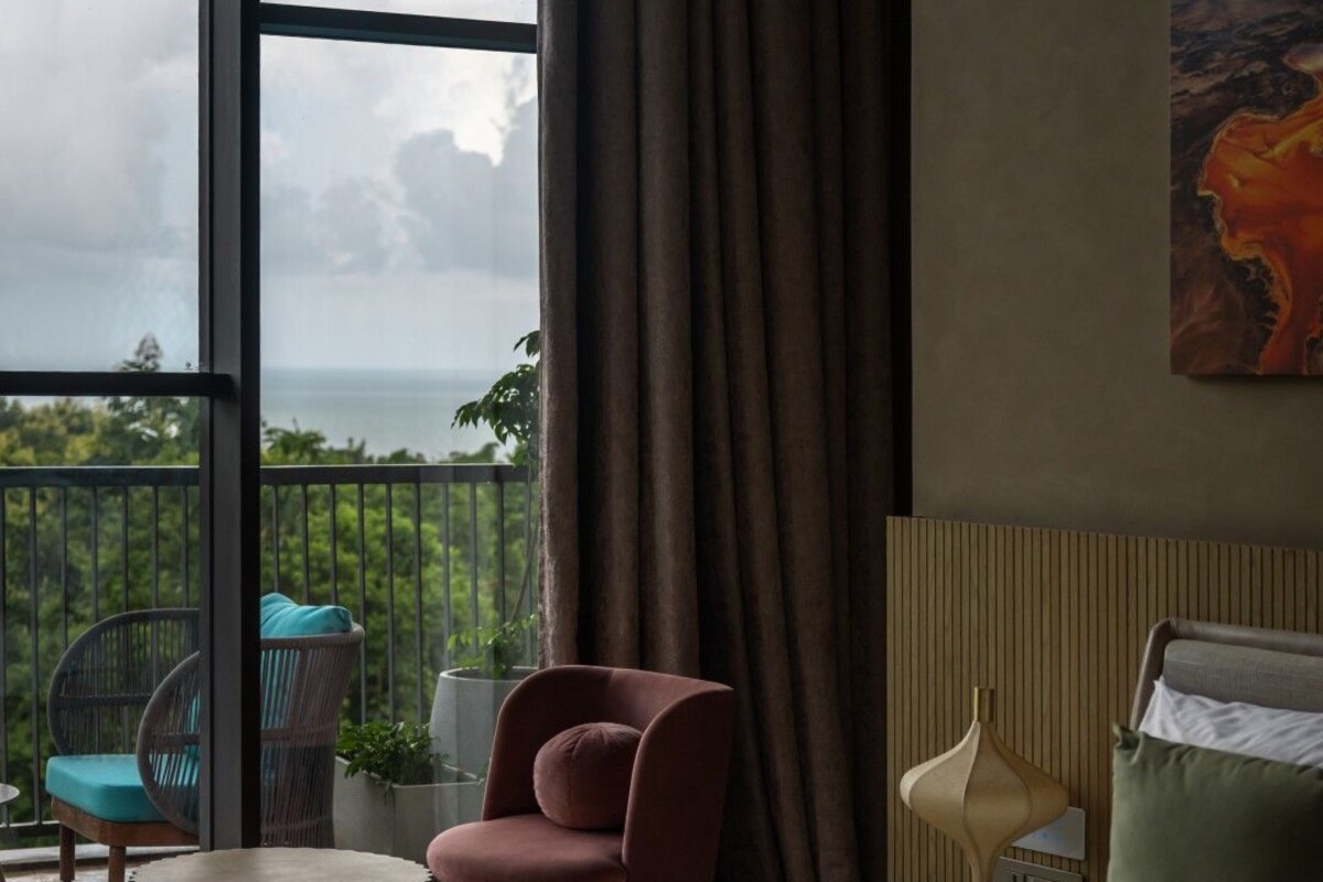 A hotel room with a bed, a chair, a small table, and a view of the outdoors.