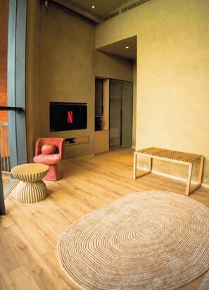 A modern living room with a flat-screen TV, a red chair, a wooden bench, and a round woven rug.