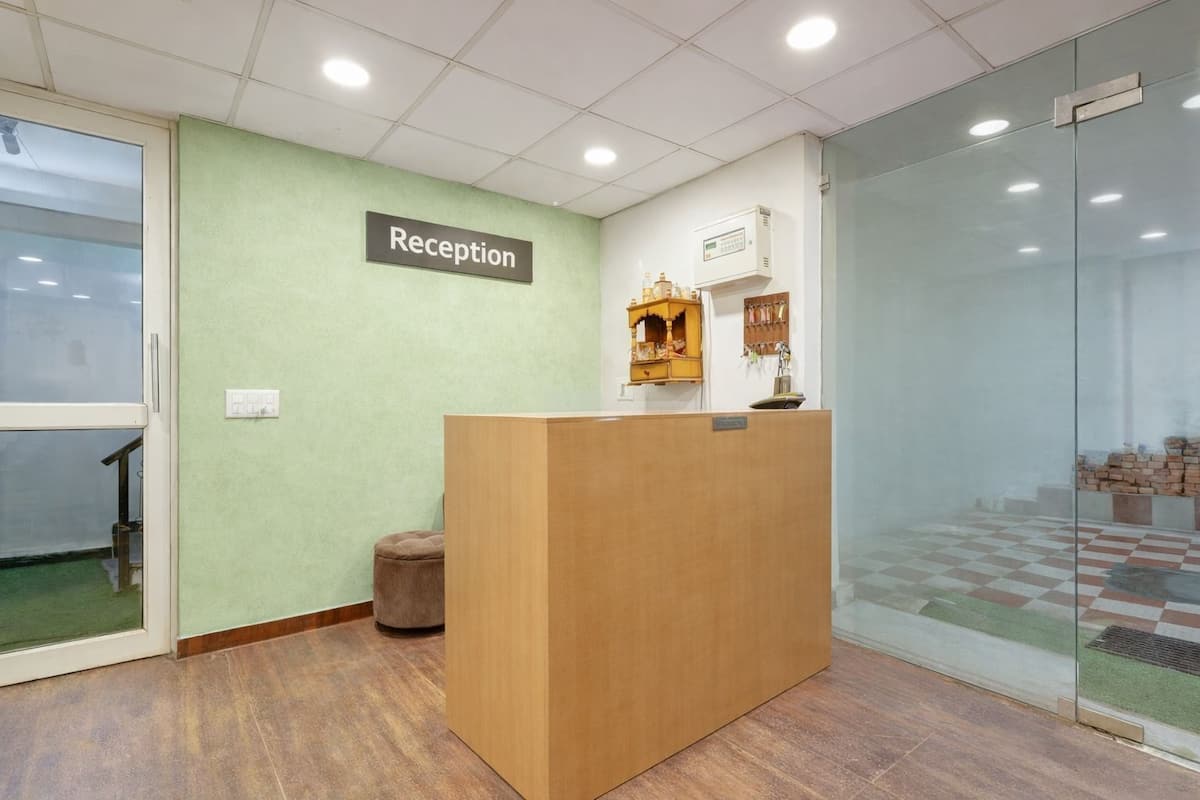 Una zona de recepción con un mostrador de madera, un cartel de recepción, un estante pequeño con objetos y una partición de vidrio.