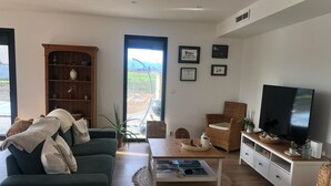 A living room with a sofa, a television, a bookshelf, and a dining table. - New house with swimming pool 10 minutes from Pau, ideal for relaxing and enjoying. (Bordes)