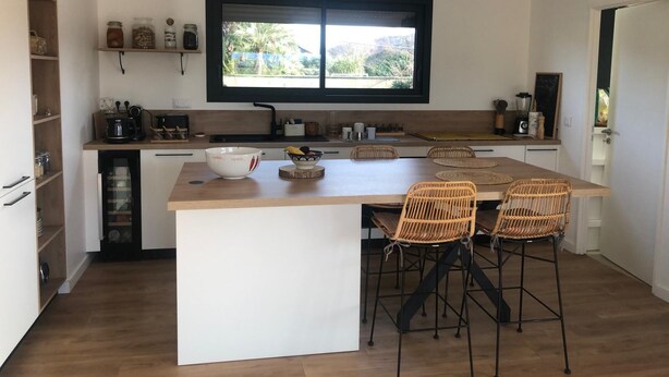 A modern kitchen with a central island, bar stools, and a window overlooking greenery. - New house with swimming pool 10 minutes from Pau, ideal for relaxing and enjoying. (Bordes)
