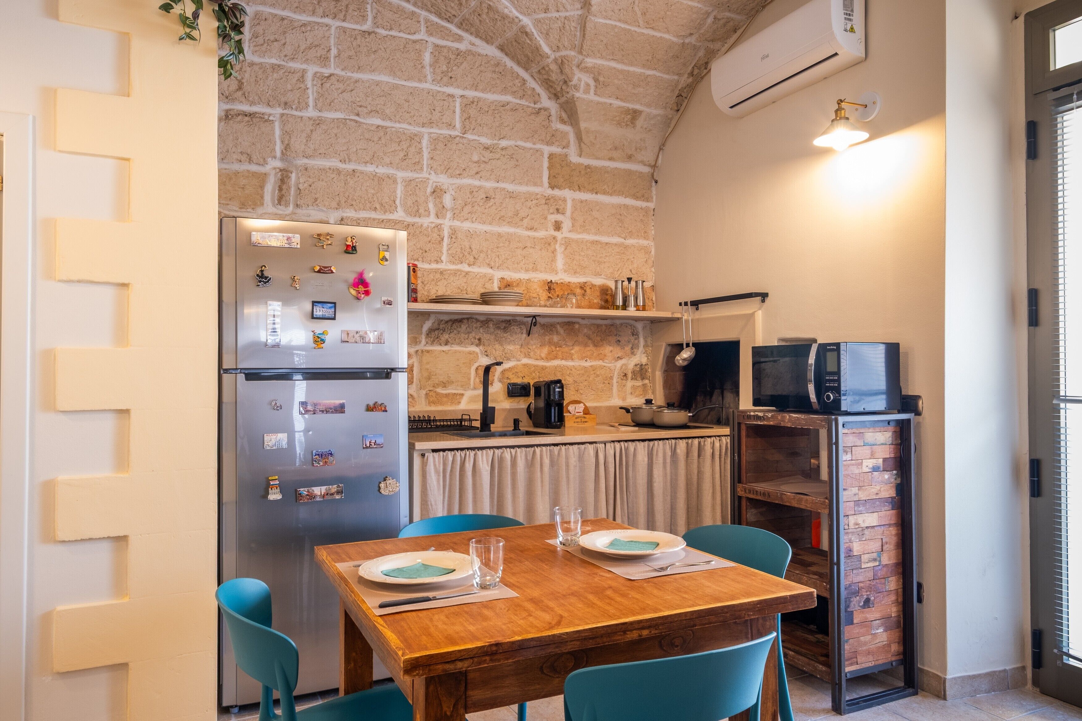Une cuisine compacte avec un mur en briques, un réfrigérateur, un four à micro-ondes et une table à manger avec des chaises.