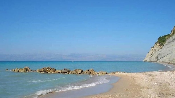 Una spiaggia costiera con cielo sereno, un litorale roccioso e una scogliera.