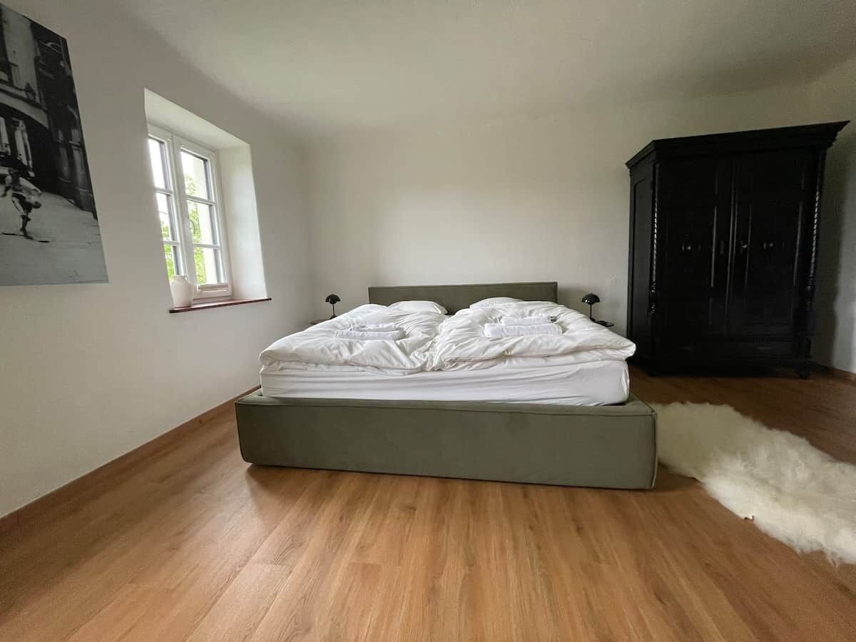 Een slaapkamer met een bed, een raam, een donkere kast en een zacht, behaard tapijt.