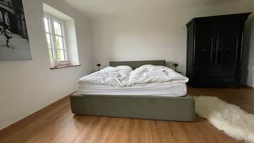 Een slaapkamer met een bed, een raam, een donkere kast en een zacht, behaard tapijt.
