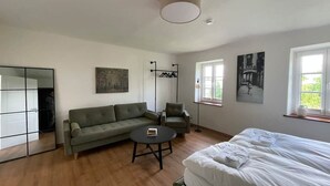 A modern room with a sofa, a chair, a bed, a round table, and artwork on the walls.