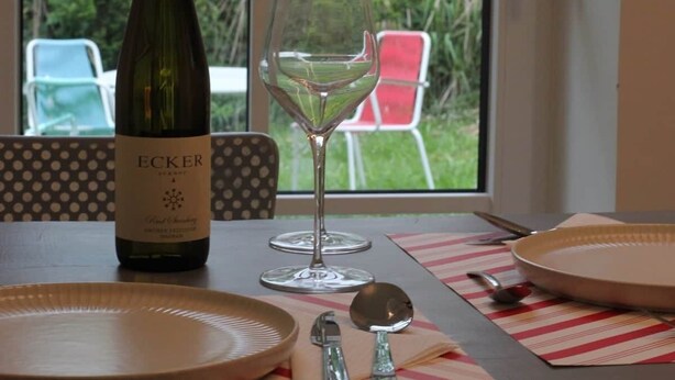 A table set with a bottle of Ecker wine, a wine glass, plates, and cutlery.