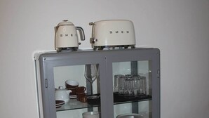 A grey cabinet with glass doors containing white dishes, glasses, and a teapot.