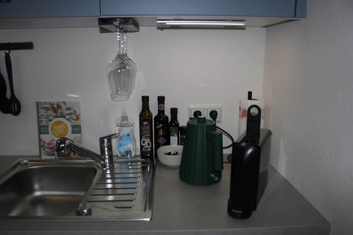 A kitchen with a sink, a wine glass holder, and various bottles.