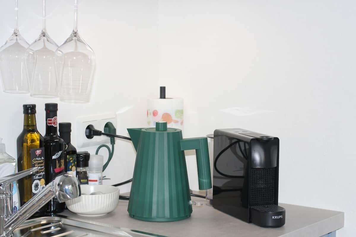 Une cuisine équipée d’une machine à café, d’une bouilloire et de diverses bouteilles.