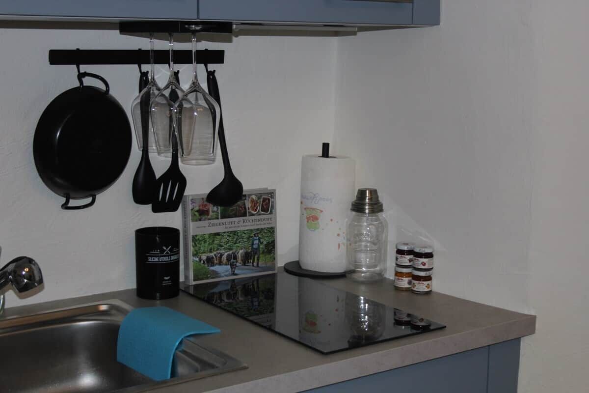 A kitchen with a sink, a stove, hanging utensils, a roll of paper towels, and a coffee maker.