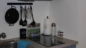 A kitchen with a sink, a stove, hanging utensils, a roll of paper towels, and a coffee maker.