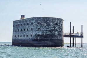 Eine zylindrische Betonkonstruktion mit mehreren Fenstern, ein Wasserturm und ein Steg, der ins Wasser führt.