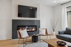 Una sala de estar moderna con una televisión de pantalla plana, chimenea, dos sillones de cuero, un sofá y una mesa de centro.