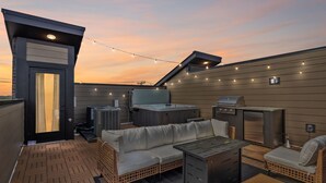 En takterrass med en bubbelpool, grill och en utomhusplats med sittmöbler.