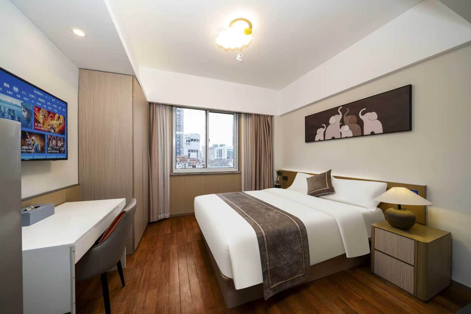 A hotel room with a bed, desk, and a city view through the window.