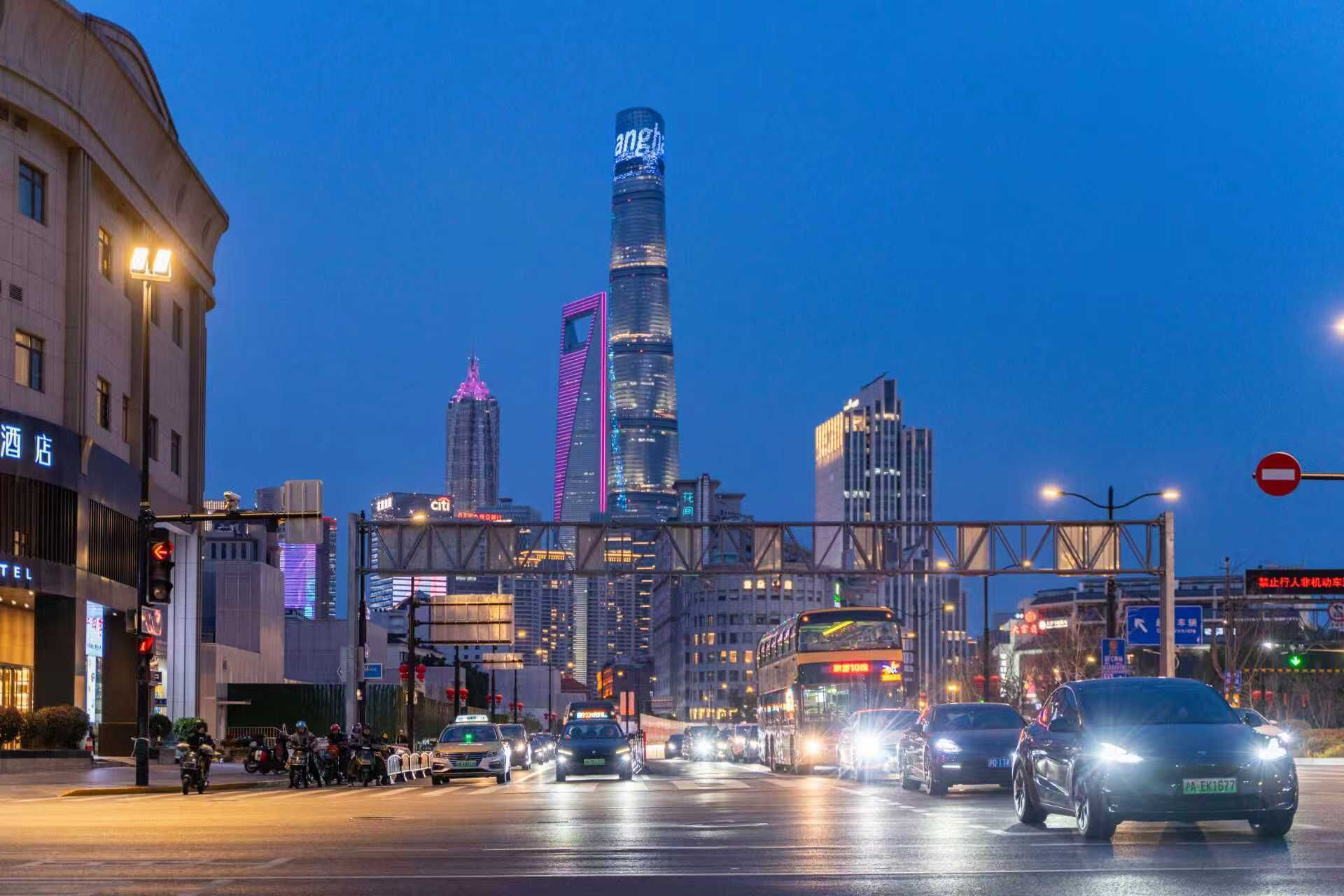 A busy urban street with modern buildings, including a prominent skyscraper with illuminated signage.