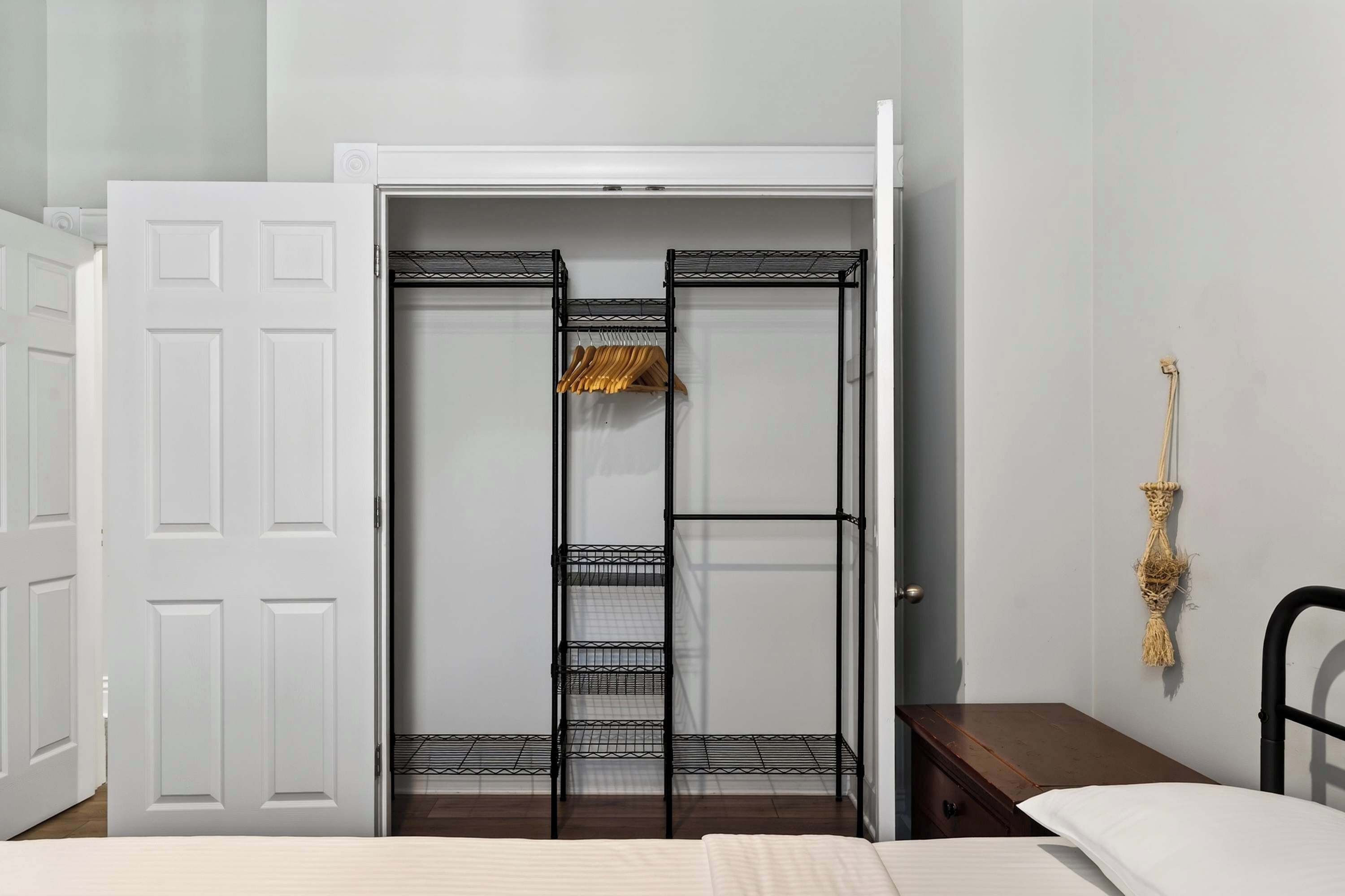 Une chambre avec une porte blanche, une étagère en métal, un lit et une petite table de chevet.