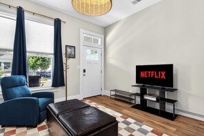 Ein Wohnzimmer mit Fernseher, blauem Sessel, einer Bank und einer Tür.