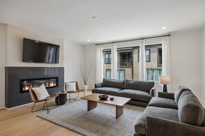 Ein modernes Wohnzimmer mit Kamin, Flachbildfernseher, grauem Sofa und Couchtisch.