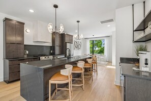 A modern kitchen with dark cabinetry, a marble island, and bar stools. - Iconic Nashville Twin Townhomes | 6BR + Hot Tubs (Nashville)
