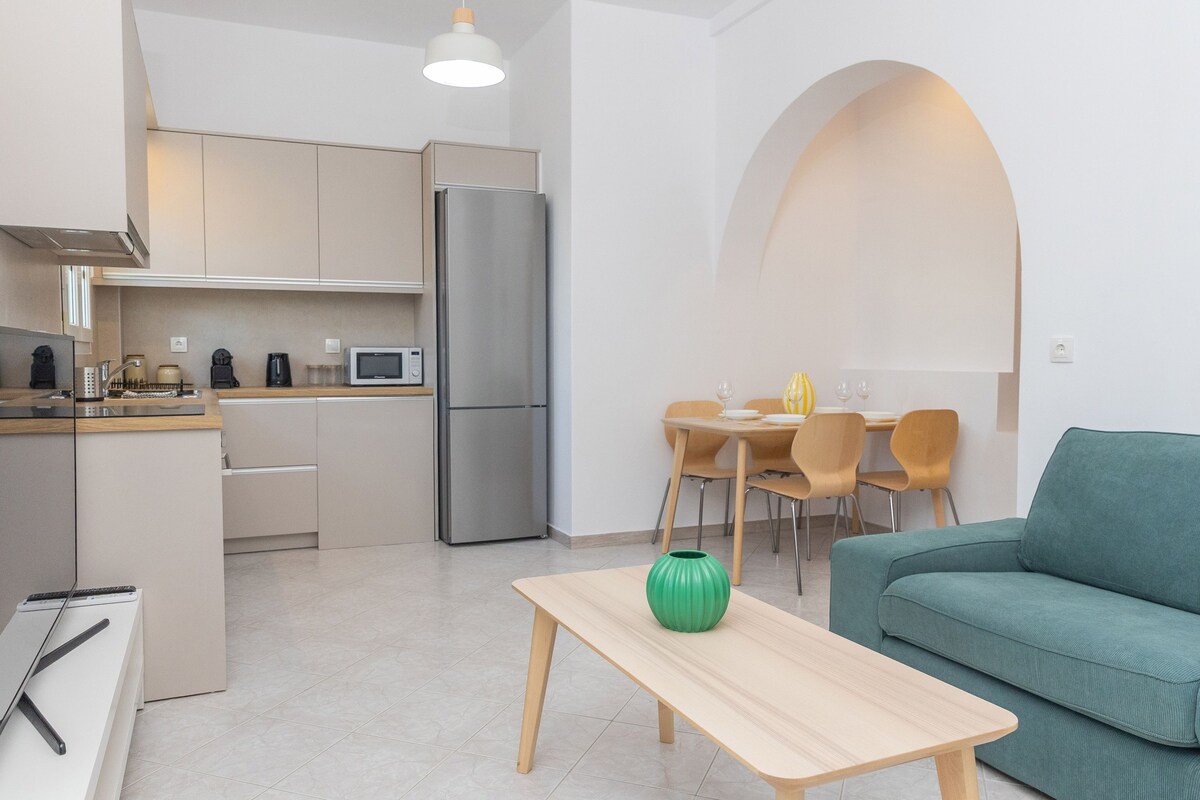 Eine moderne Küche mit Kühlschrank, Mikrowelle und Kaffeemaschine. Es gibt einen Essbereich mit Tisch und Stühlen sowie ein grünes Sofa.