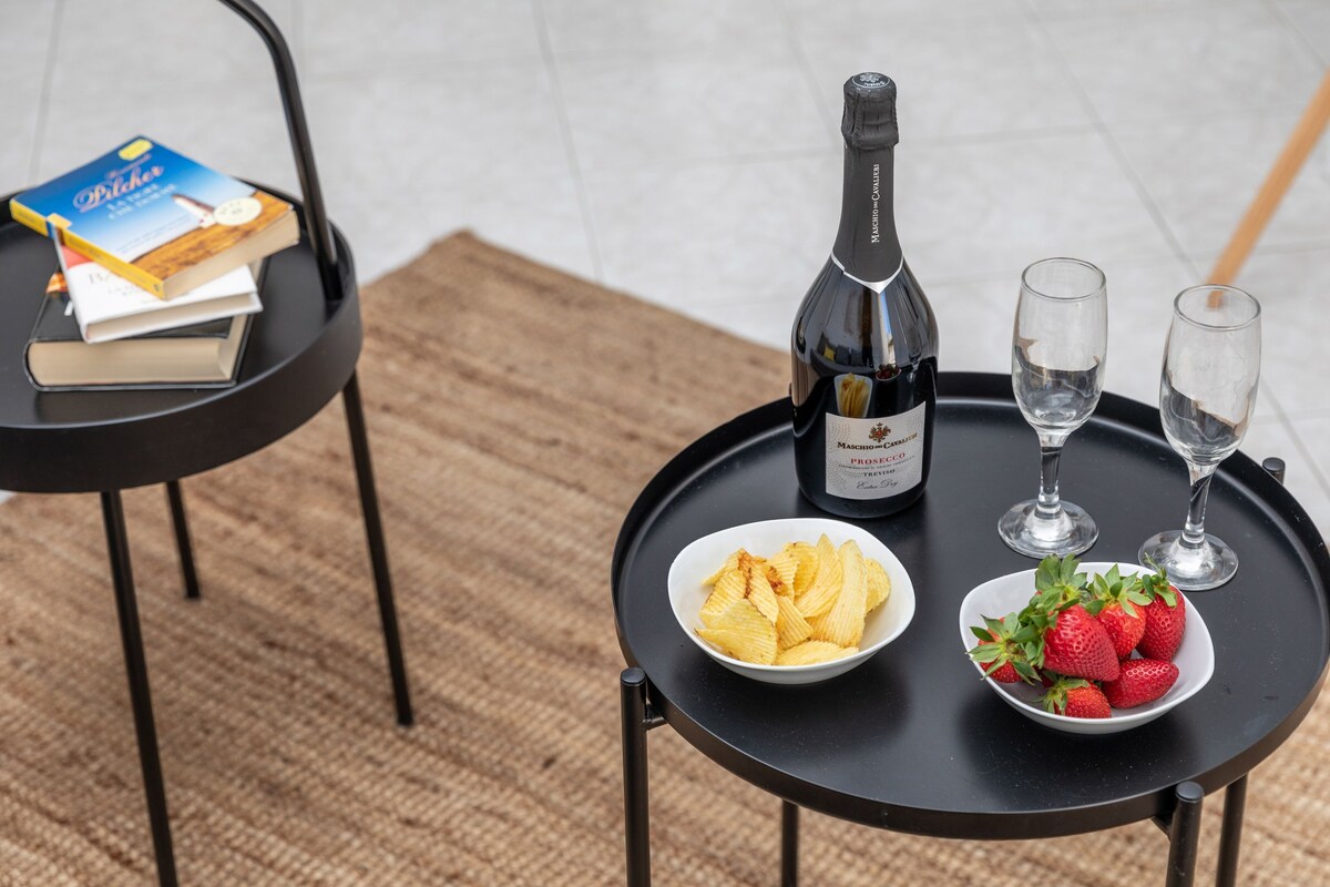 Ein kleiner runder Tisch mit einer Champagnerflasche, zwei Gläsern, einer Chips-Schale und einer Schale Erdbeeren.