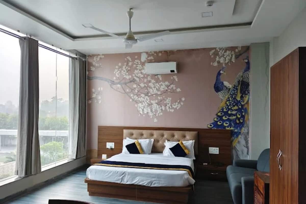 Ein Hotelzimmer mit einem großen Bett, einem Pfauen-Wandgemälde und Blick aus dem Fenster.
