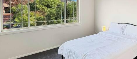 Un dormitorio con un ventanal grande, una cama y una mesita de noche.