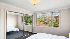 A bedroom with a bed, a mirror, and large windows with a view of the outside. - Metawise Spacious 4-bedroom Home in Cherrybrook (Sydney)