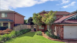 A residential house with a brick exterior, a front yard with a lawn, a garage, and a tree. - Metawise Spacious 4-bedroom Home in Cherrybrook (Sydney)