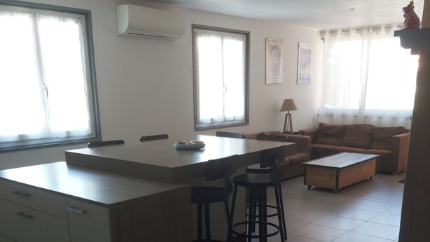 A modern kitchen with a central island, bar stools, a sofa, and a dining table. - 2-bedroom apartment with terrace 5 minutes from the center and beaches (Collioure)