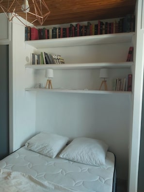 Ein Schlafzimmer mit einem Bett, zwei Nachttischen, einem Bücherregal und einer Pendelleuchte.