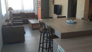 A modern kitchen with a central island, bar stools, a sofa, and a television. - 2-bedroom apartment with terrace 5 minutes from the center and beaches (Collioure)