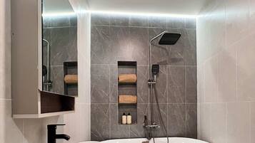Un baño moderno con una bañera independiente, un lavabo redondo y un cabezal de ducha.