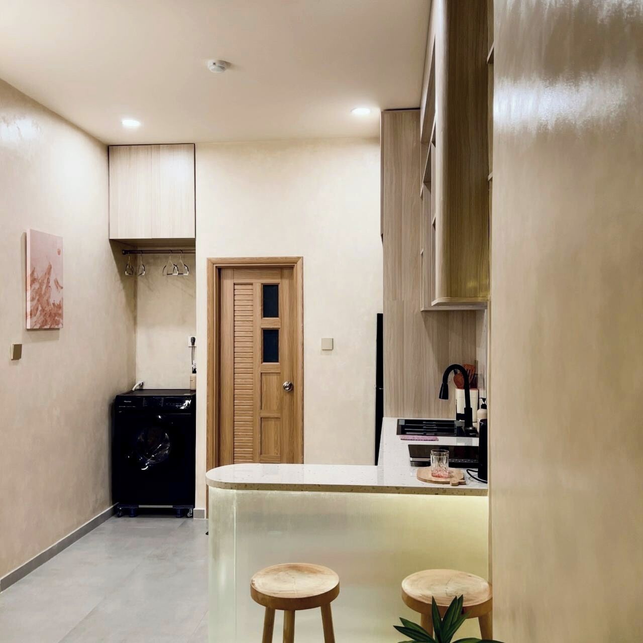 Una cocina compacta con una isla central, dos taburetes y una puerta de madera.
