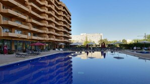 Un hotel con una piscina amplia, varios balcones y un cielo despejado.