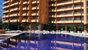 Un hotel con una piscina grande, mobiliario exterior y varios balcones.